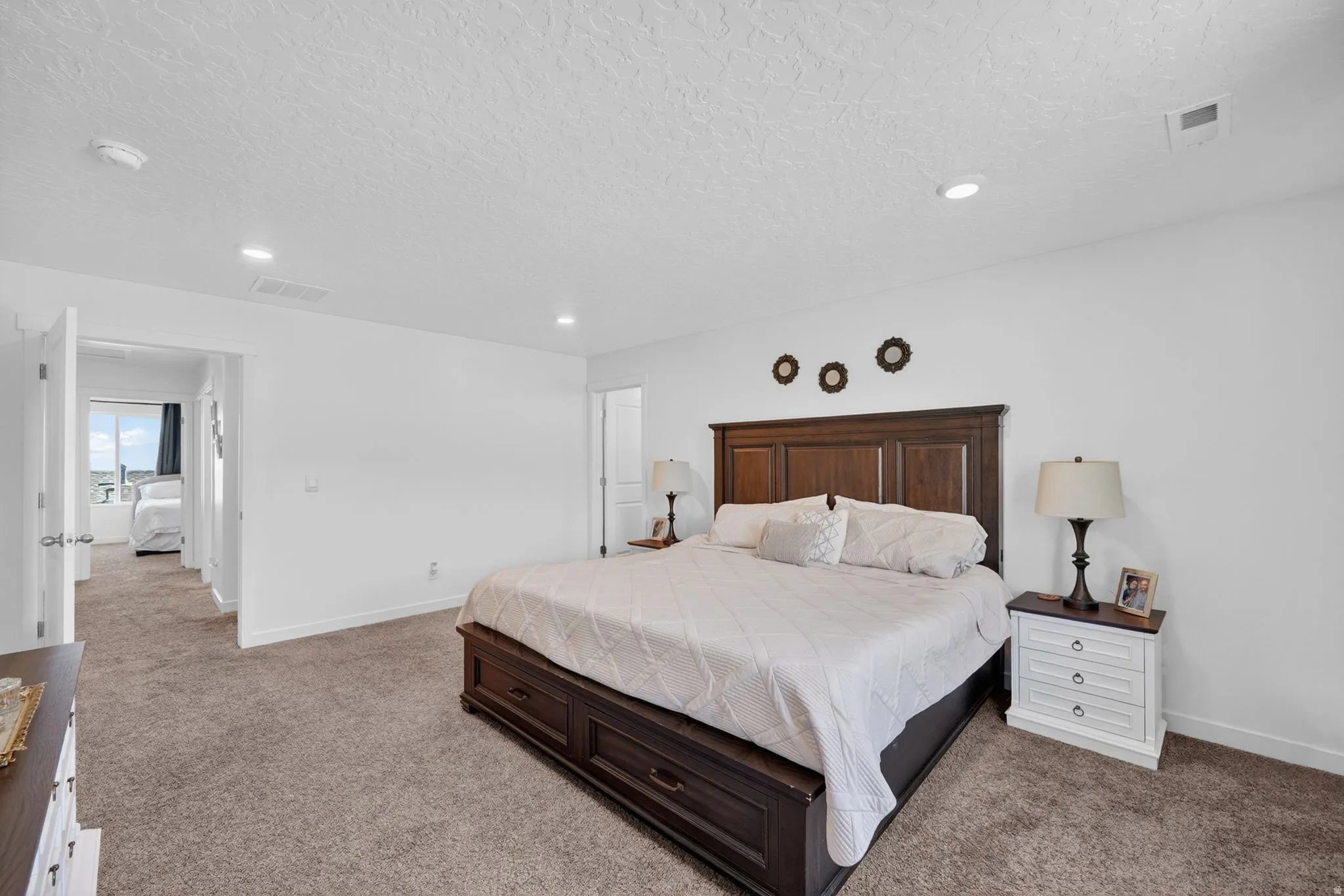 Spacious bedroom featuring neutral carpeting, recessed lighting, and a white color palette