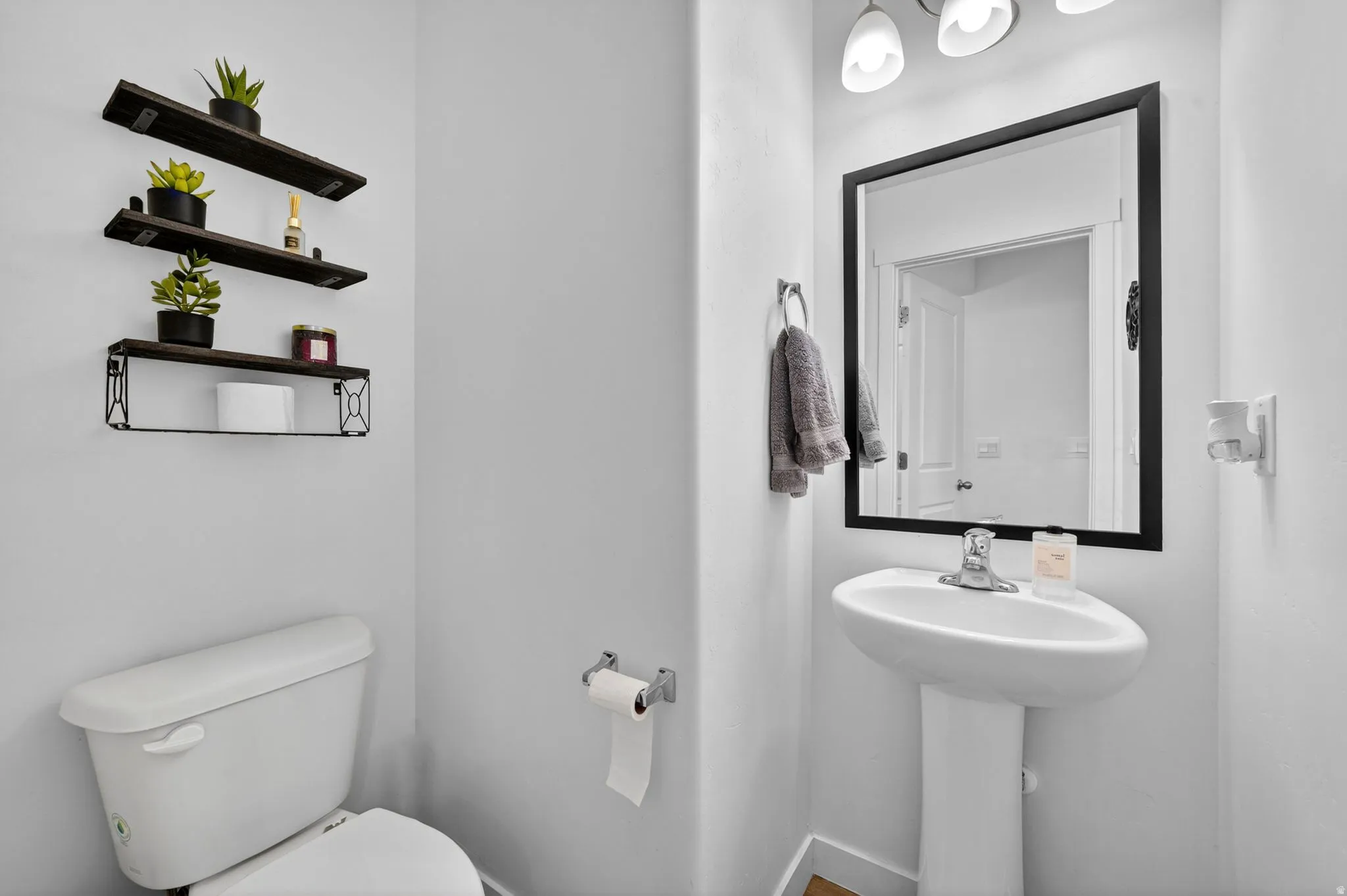 Pedestal sink with a polished chrome faucet, framed by a rectangular mirror with a black border