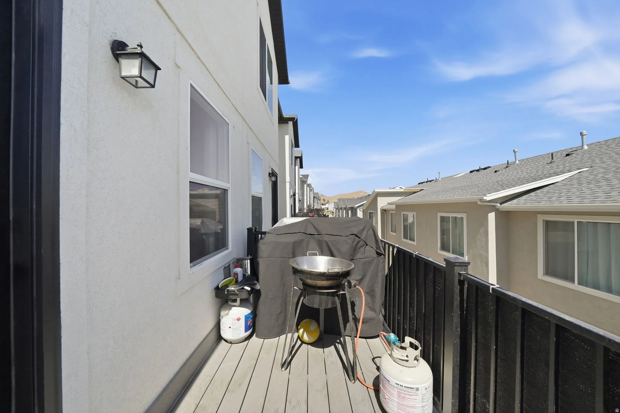 Outdoor balcony featuring composite decking, black metal railing, and a stucco exterior with an exterior light fixture