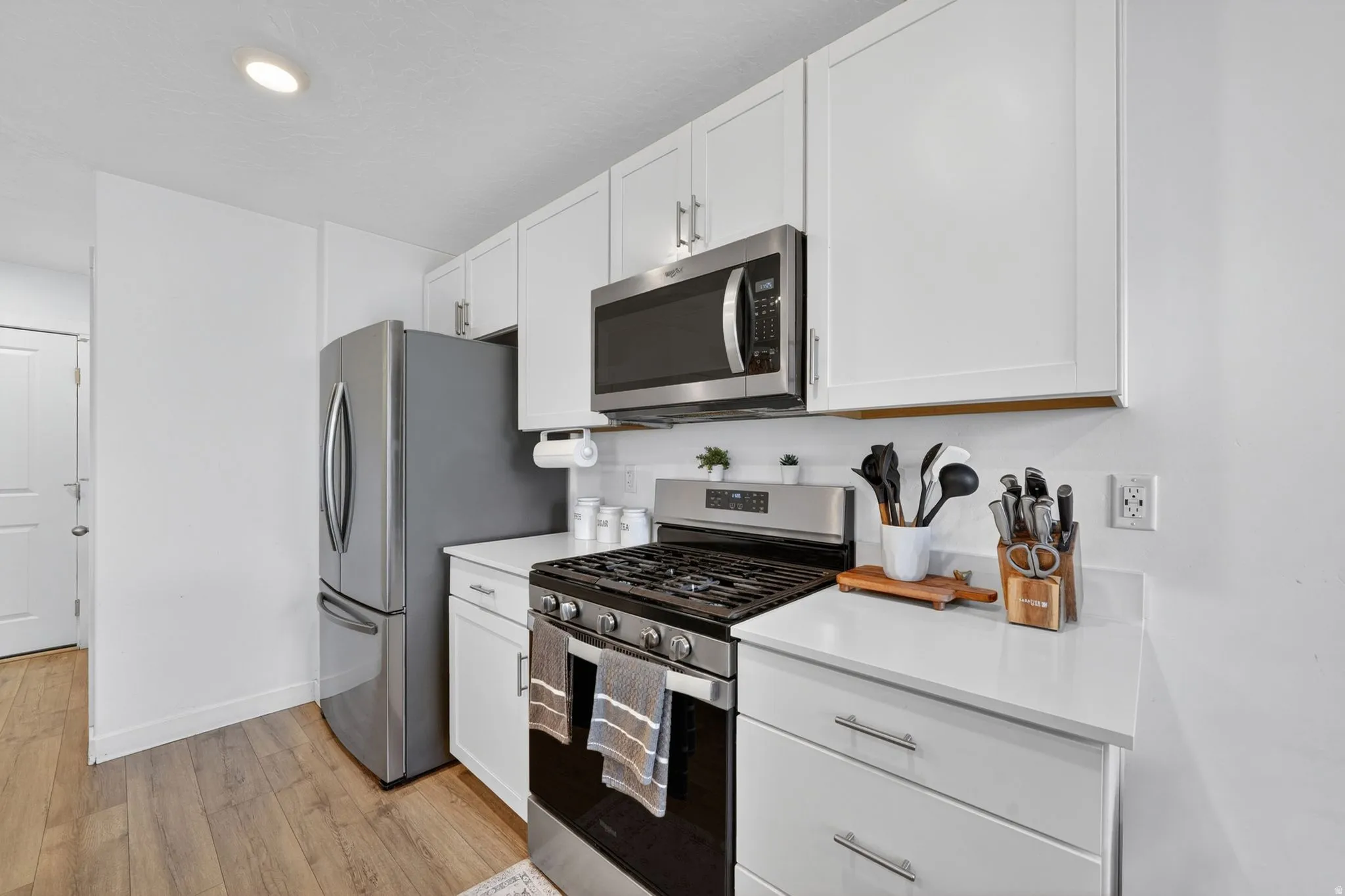 Contemporary kitchen featuring white cabinetry, stainless steel appliances, light countertops, a gas range, and wood-finish flooring