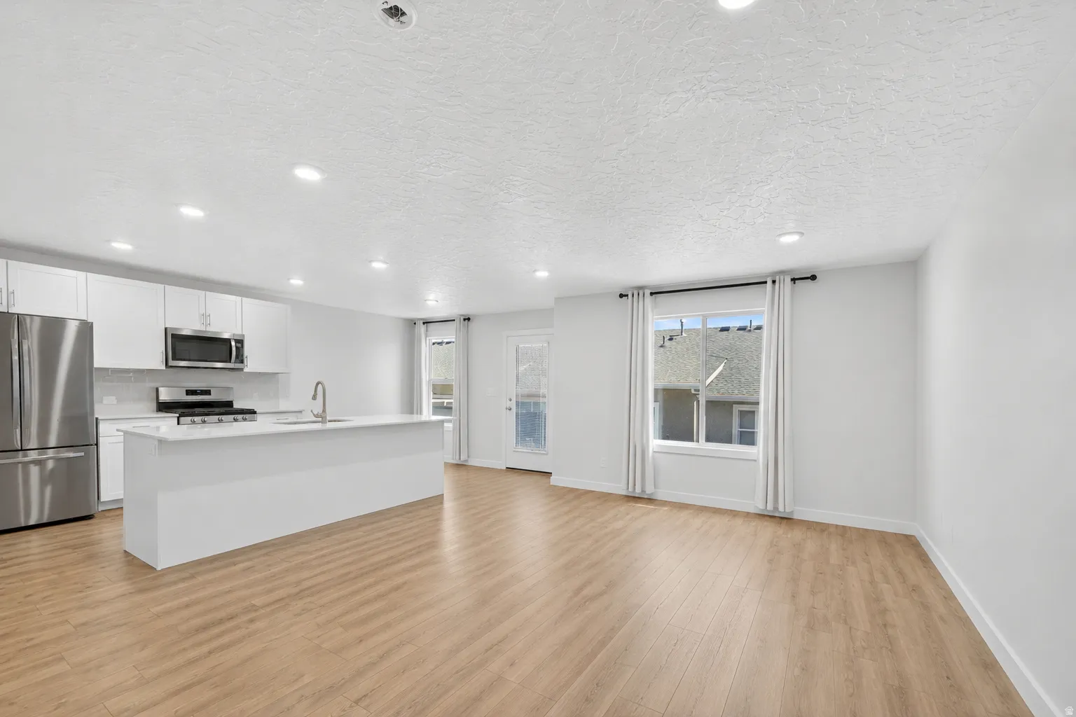 Contemporary open-concept living space featuring light wood-finish flooring, recessed lighting, and white walls