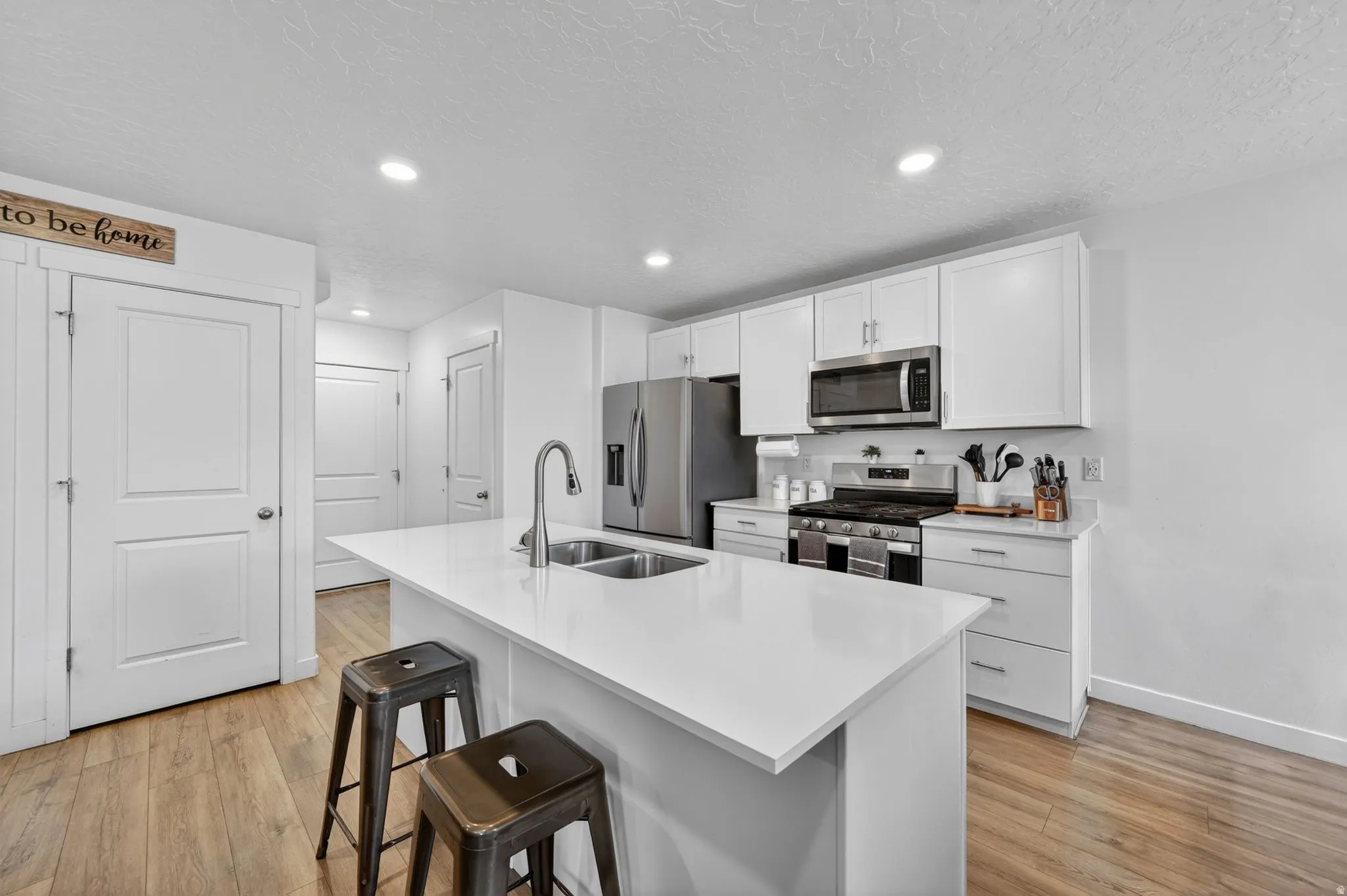 Kitchen featuring a central island with dual basin sink, wood-finish flooring, white cabinetry, recessed lighting, and stainless steel appliances