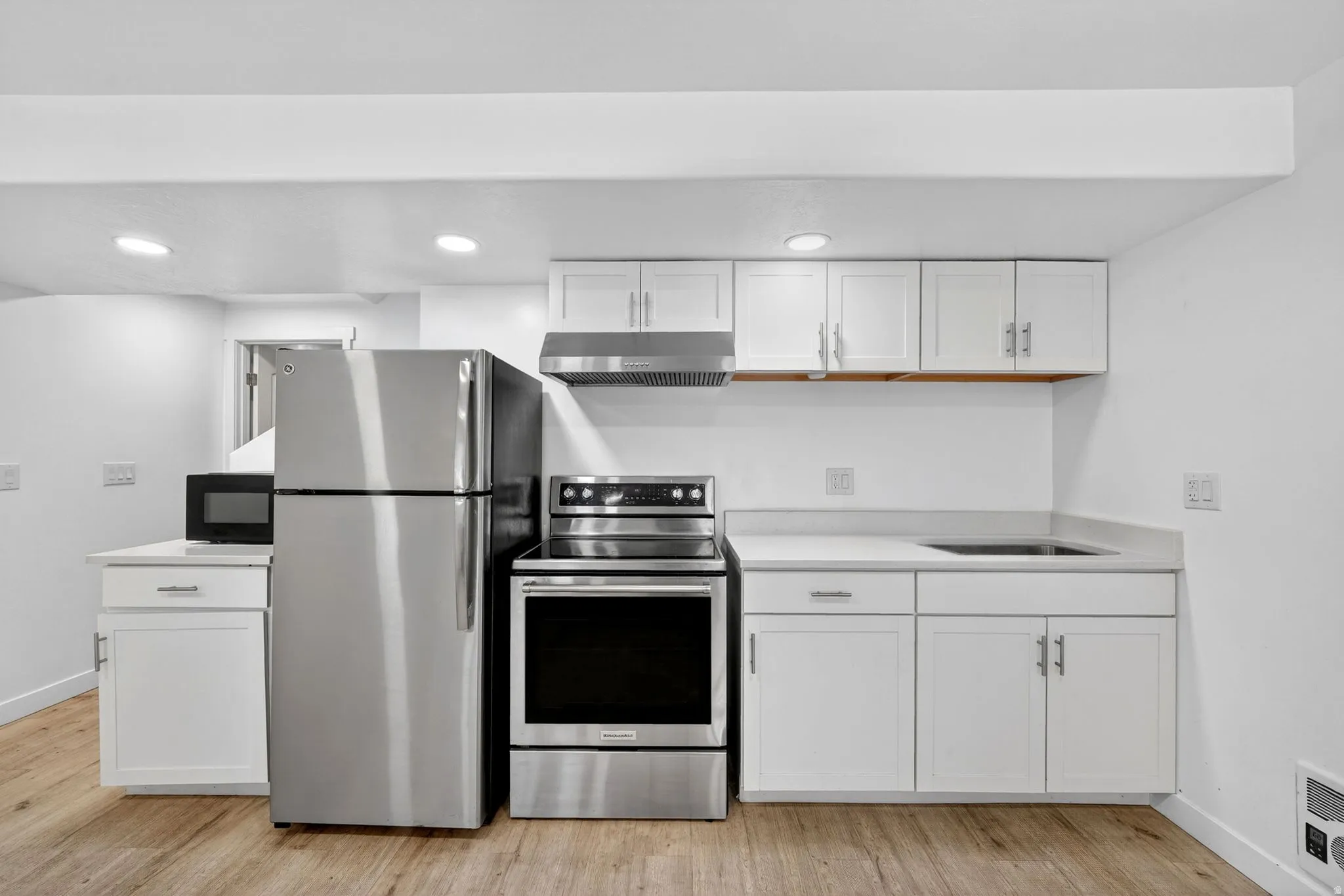 Kitchenette featuring stainless steel appliances, white cabinetry, a built-in sink, recessed lighting, and wood-finish flooring