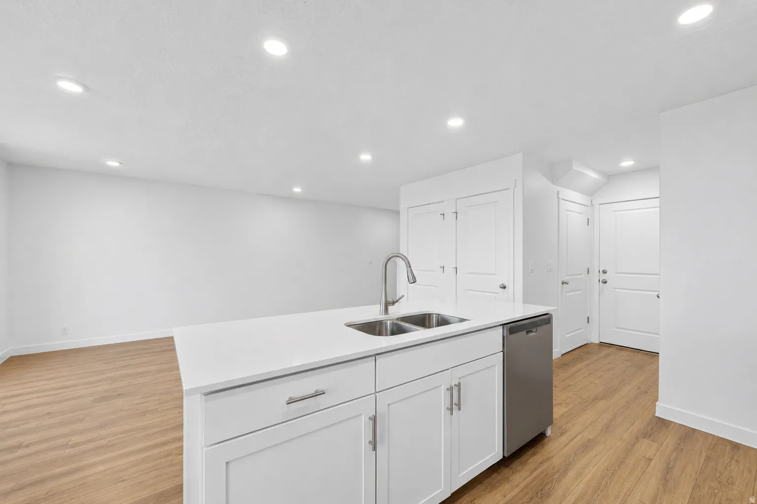 Kitchen island featuring a double-basin stainless steel sink with a high-arc faucet, integrated dishwasher, and white shaker-style cabinetry