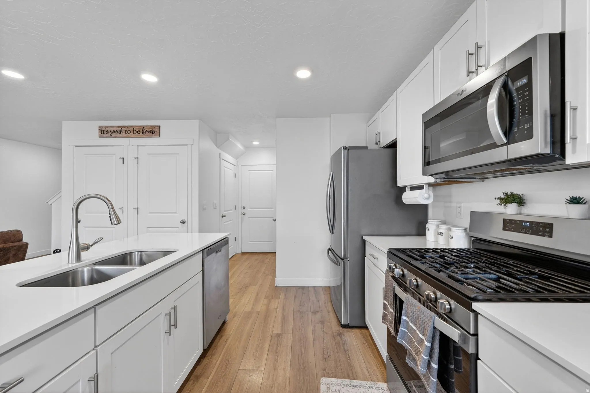 Modern kitchen featuring white shaker cabinetry, stainless steel appliances, a center island with double basin sink, light countertops, and wood-finish flooring
