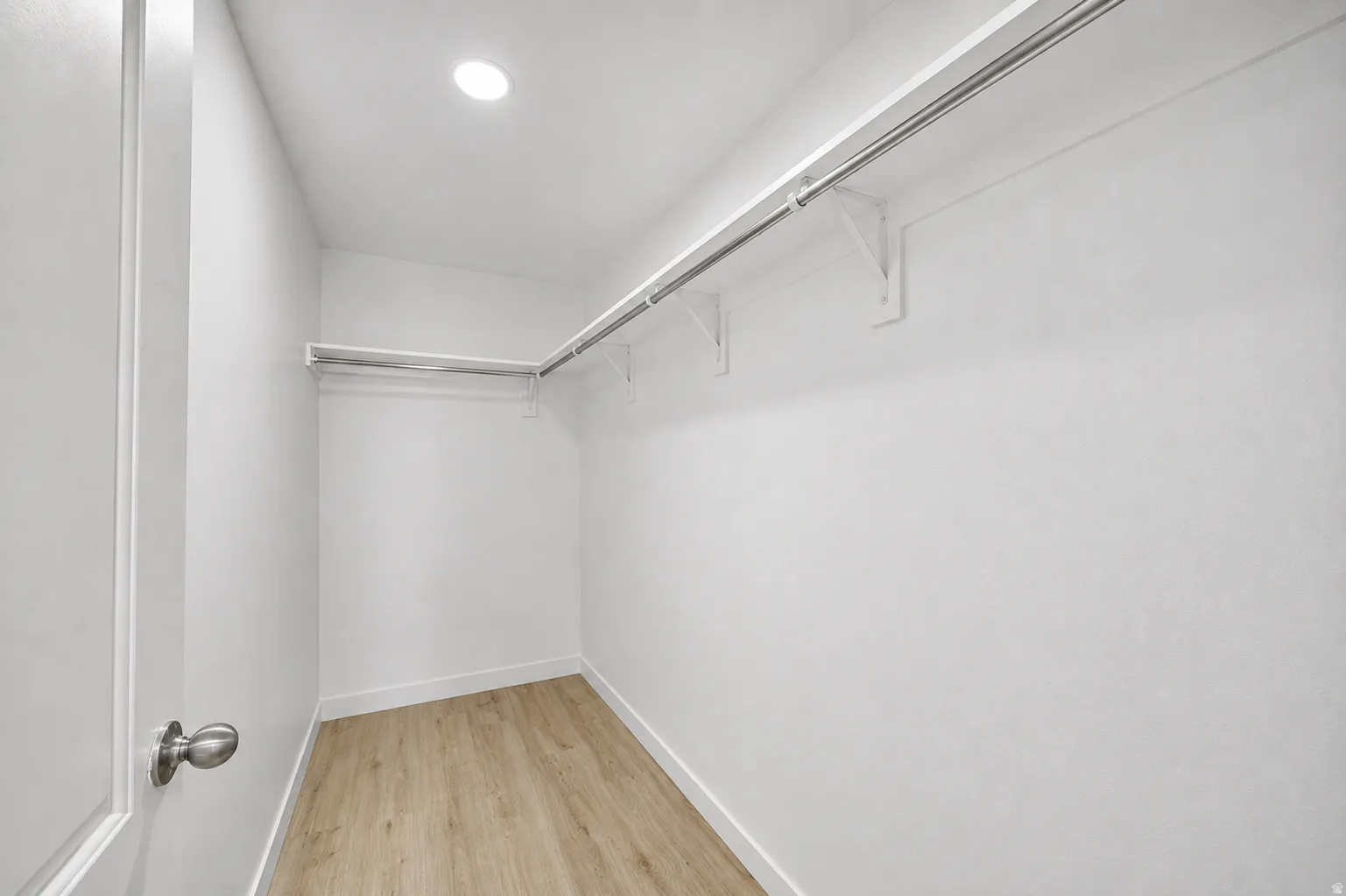 Bright walk-in closet featuring light wood-finish flooring, white walls, and recessed lighting