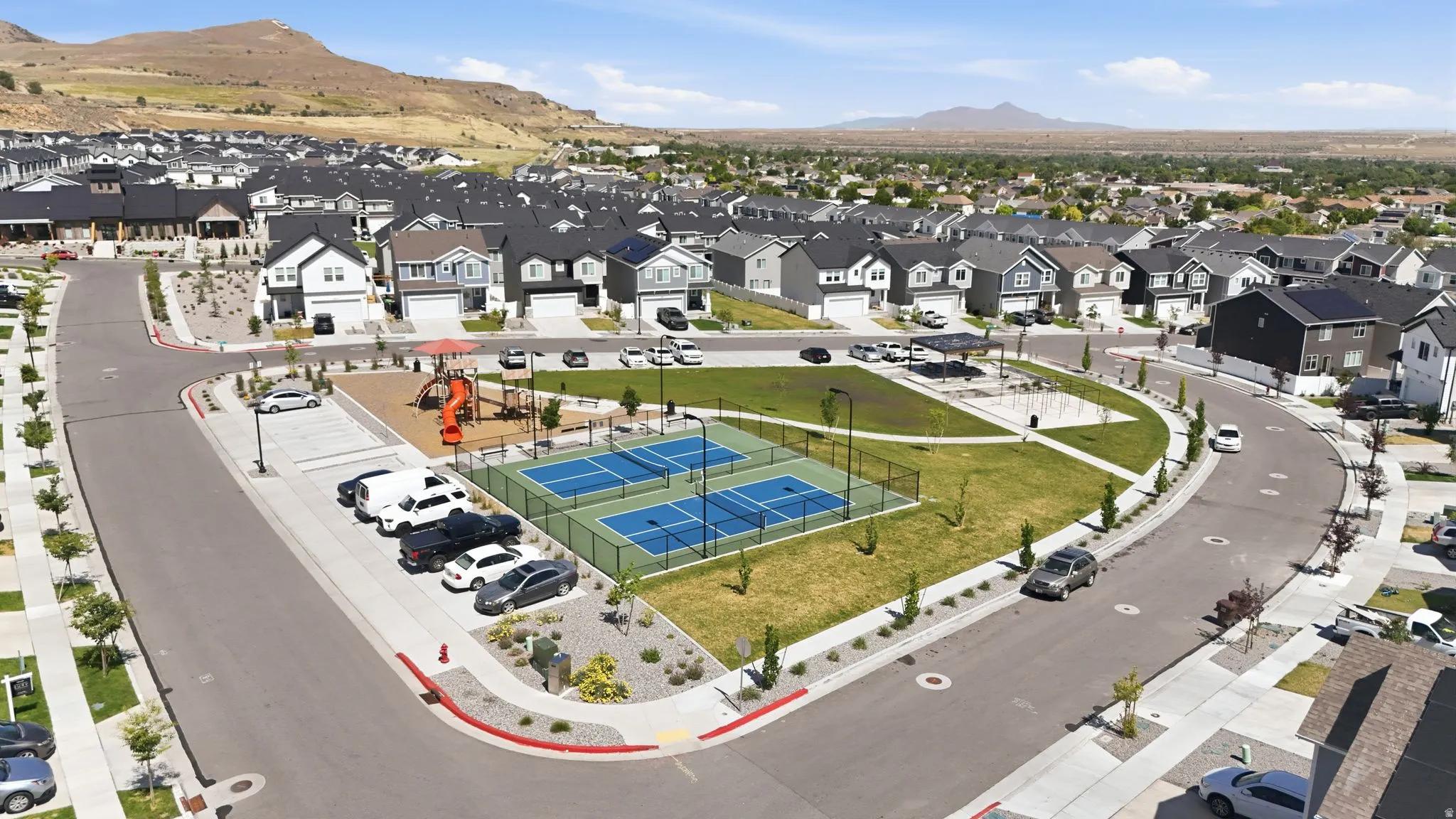 Community green space featuring two fenced pickleball courts, a children's play structure, and a covered picnic area
