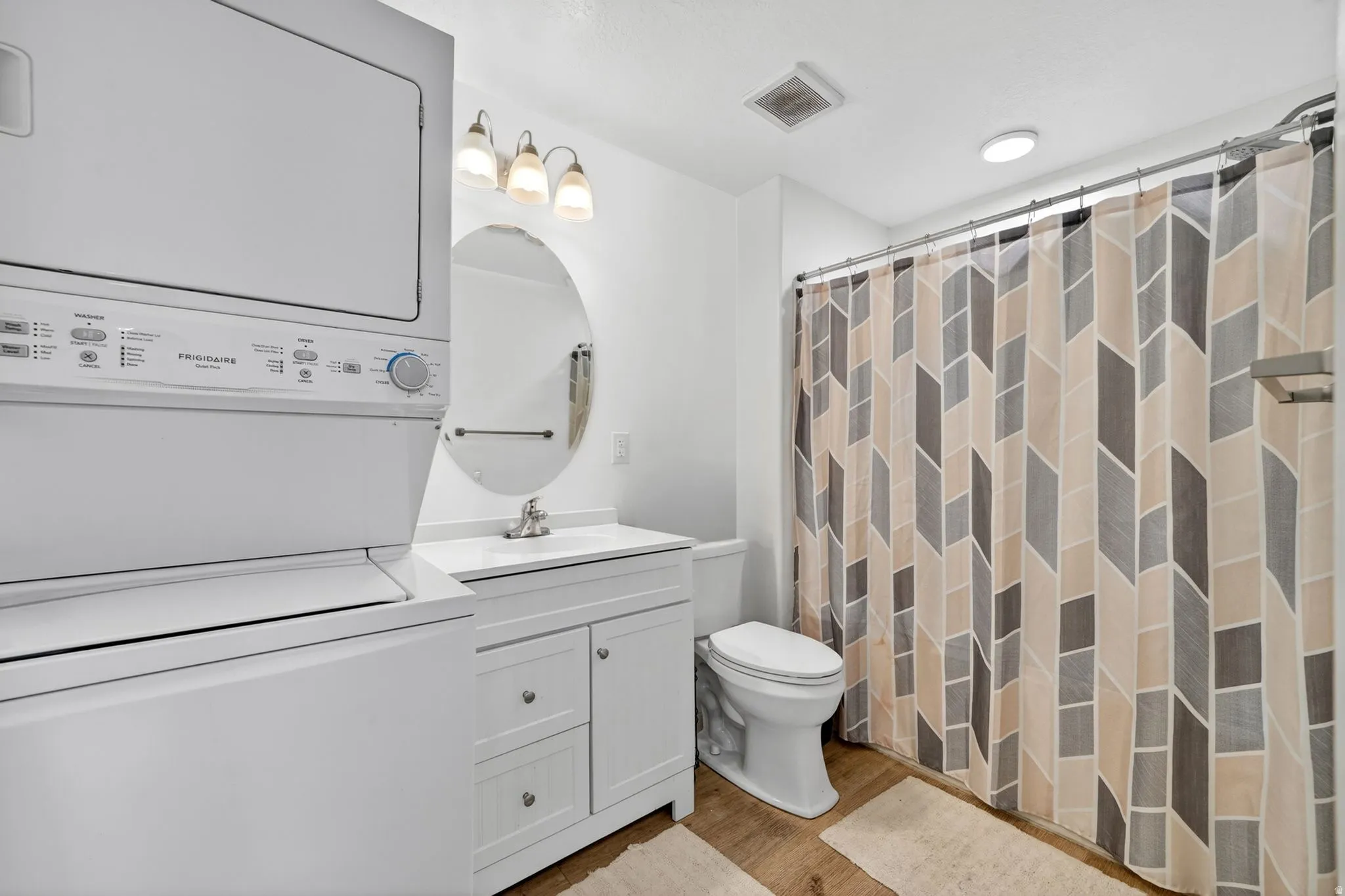 Bathroom featuring a stacked washer and dryer, single vanity with white cabinetry, oval mirror, and a full shower with patterned curtain