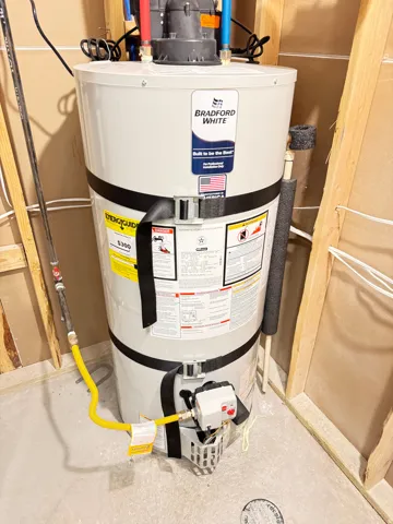 Bradford White water heater featuring a yellow gas line connection, PEX hot and cold water lines, and a visible drain