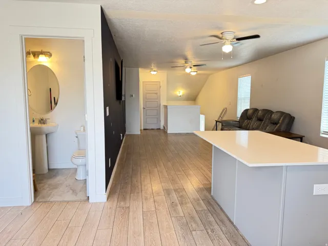 Open-concept living space featuring wood-finish flooring, a white countertop island, and multiple ceiling fans