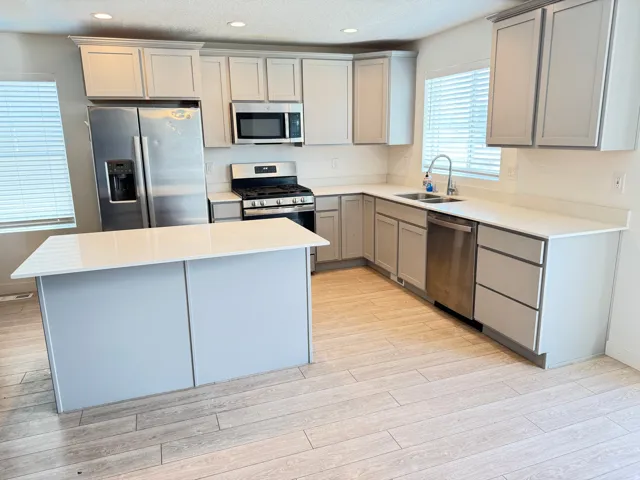 Modern kitchen featuring an island, light gray cabinetry, white countertops, stainless steel appliances, and wood-finish flooring