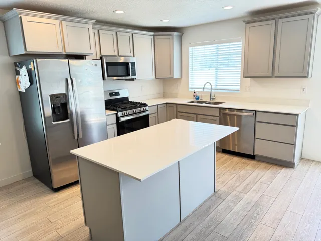 Kitchen featuring light gray cabinetry, stainless steel appliances, a center island with a white countertop, and wood-finish flooring