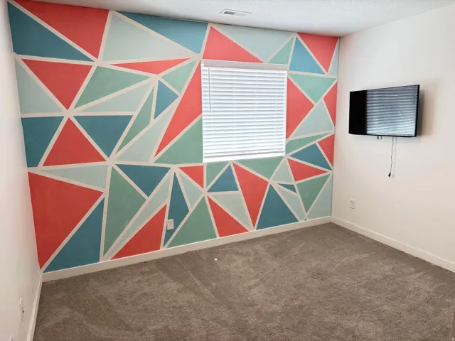 Room featuring a multi-color geometric accent wall, a single window with horizontal blinds, and neutral carpeting