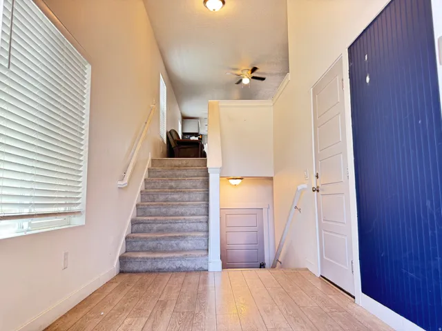 Entryway featuring wood-finish flooring, a carpeted staircase with a white handrail, and a white four-panel door
