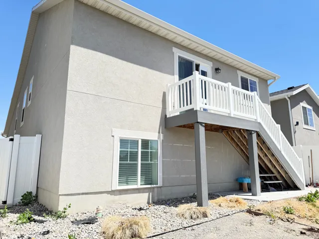 Exterior stucco finish featuring a second-story balcony with white railings, a sliding glass door, a privacy fence, and a ground-level window