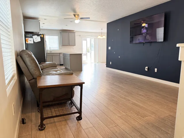 Open-concept living area featuring wood-finish flooring, a dark accent wall, and a ceiling fan