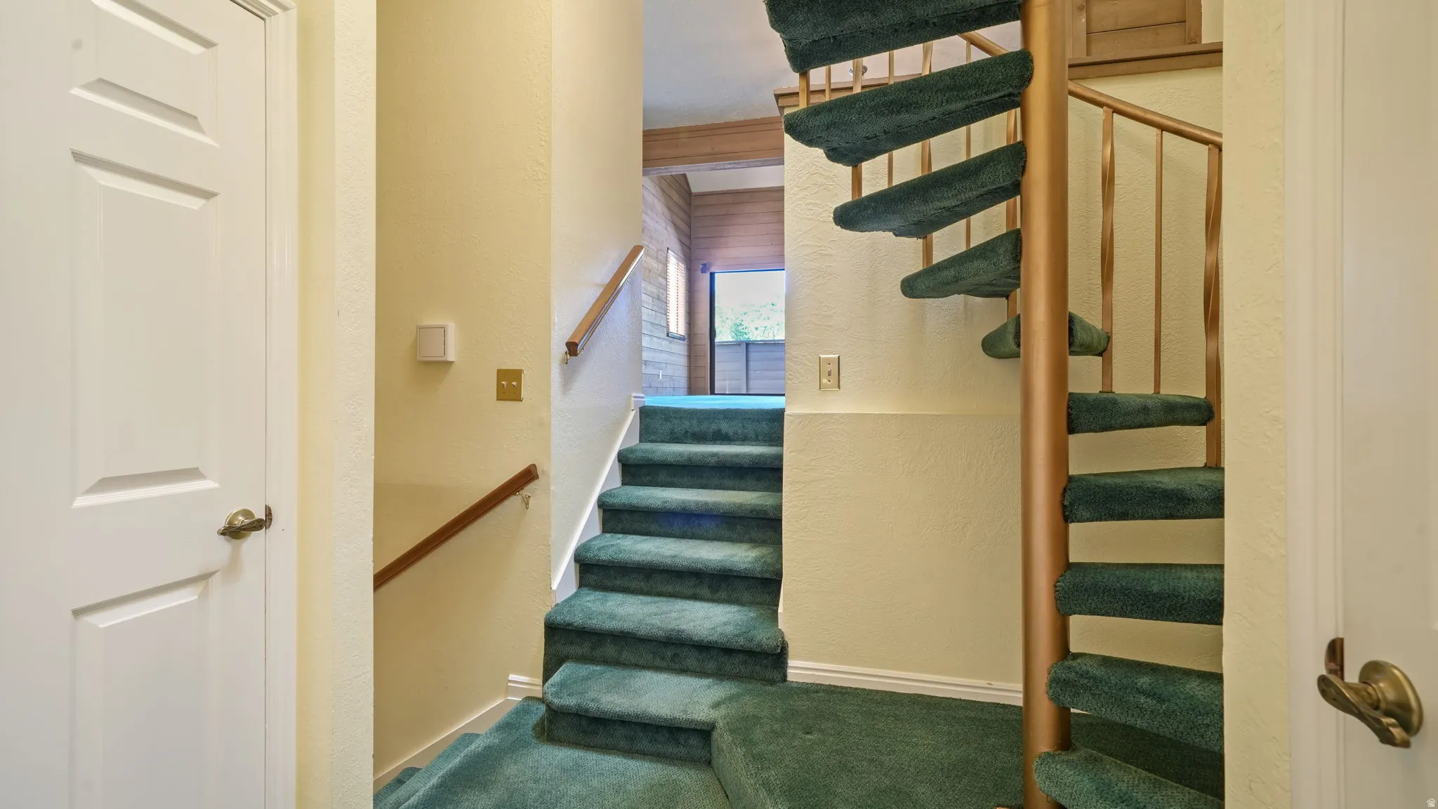 Dual staircase configuration featuring a straight carpeted stairwell with wood railing and a spiral staircase with carpeted treads and a metal banister