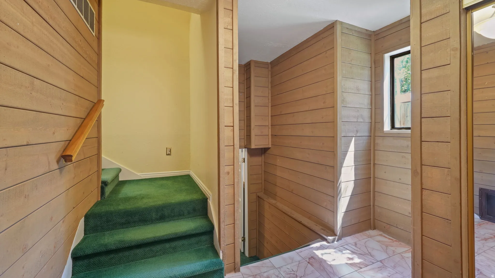 Carpeted staircase with wood-finish handrail, horizontal wood-paneling accents, a small window, and tile flooring