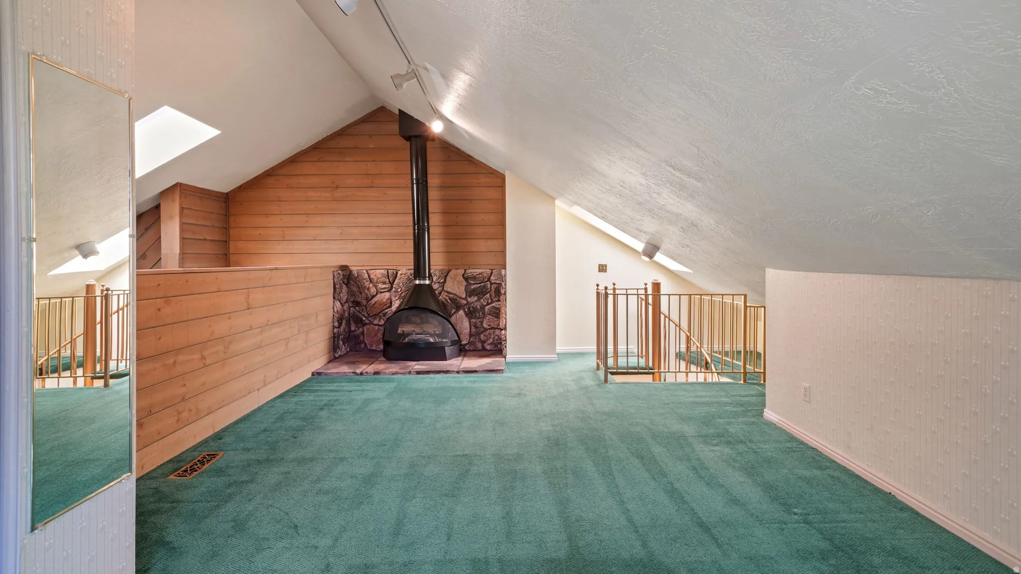Loft area featuring a freestanding metal fireplace with a stone hearth, wood paneled walls, skylights, and sloped ceilings