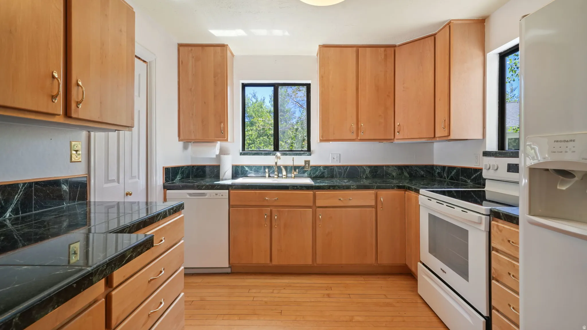 Kitchen featuring wood-finish cabinetry, dark stone countertops, wood-finish flooring, and white appliances