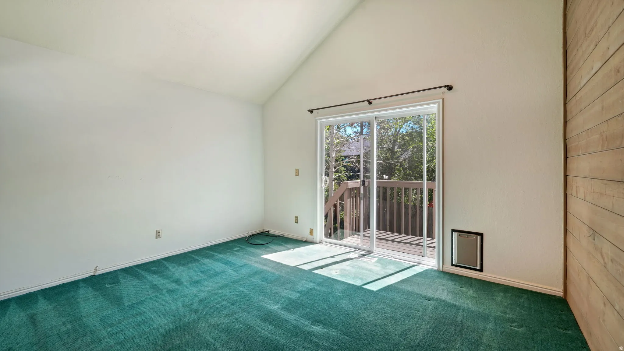 Room featuring a vaulted ceiling, green carpeting, and a wood-paneled accent wall