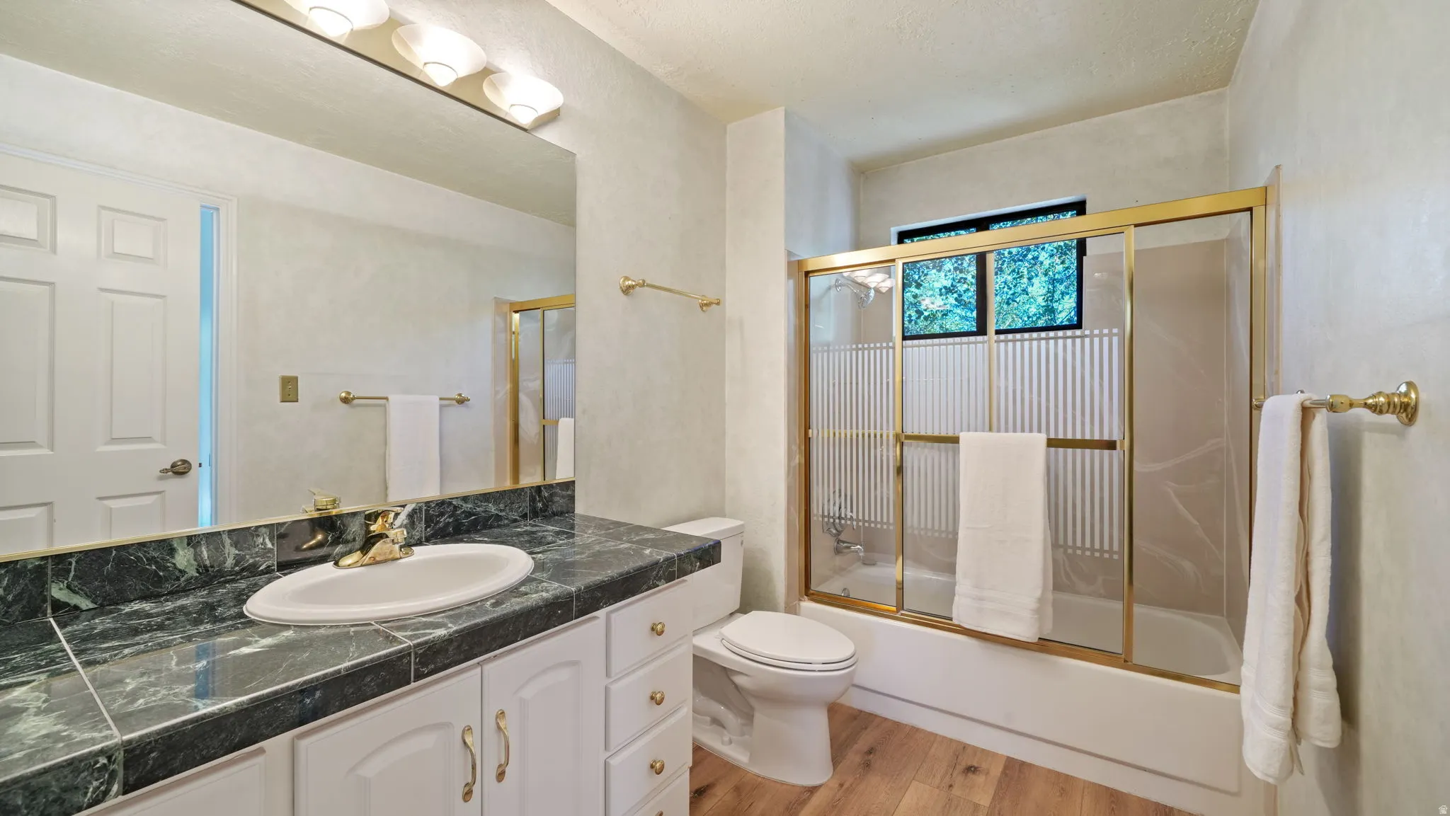 Bathroom featuring a dark stone countertop with integrated sink, white cabinetry, and a gold-framed shower/tub combination with frosted panels