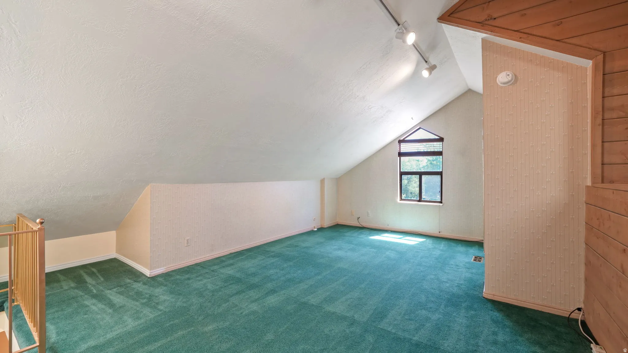 Spacious loft area featuring a peaked ceiling, an angular window, and track lighting