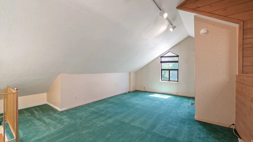 Spacious loft area featuring a peaked ceiling, an angular window, and track lighting