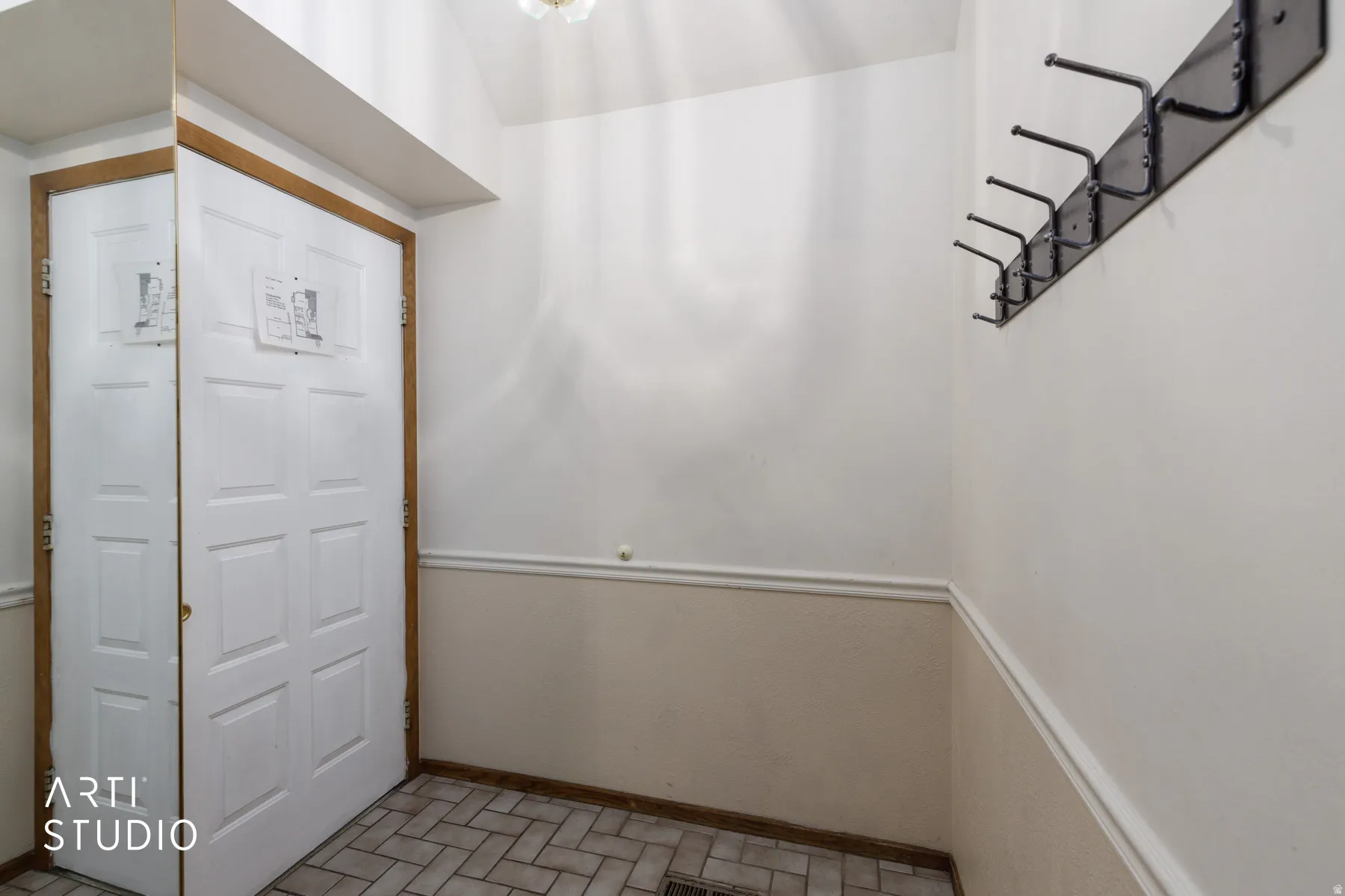 Entryway featuring a paneled door with wood-finish trim, herringbone tile flooring, wainscoting, and a wall-mounted coat rack