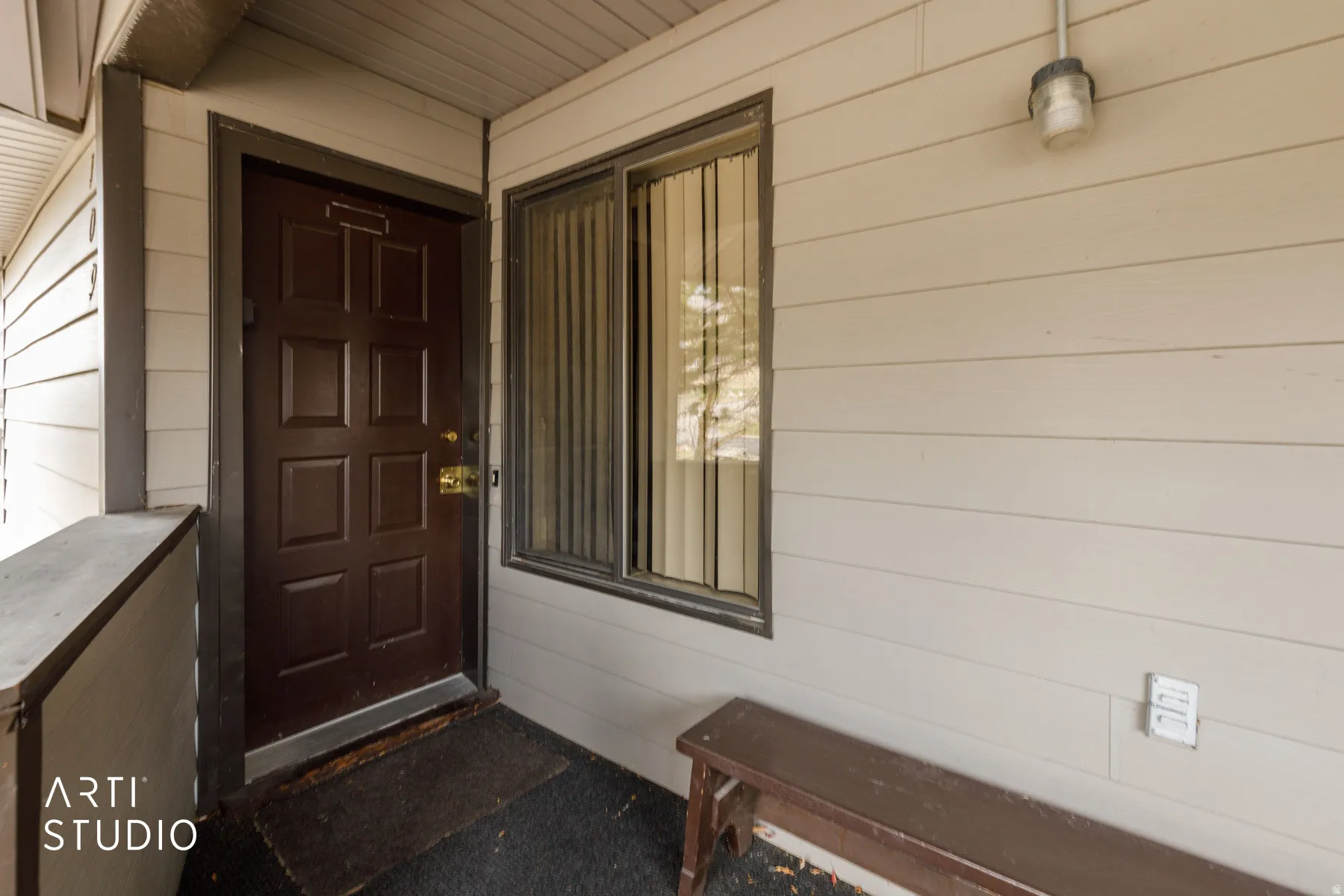 Entryway featuring a paneled door with brass hardware, adjacent window with vertical blinds, and horizontal siding