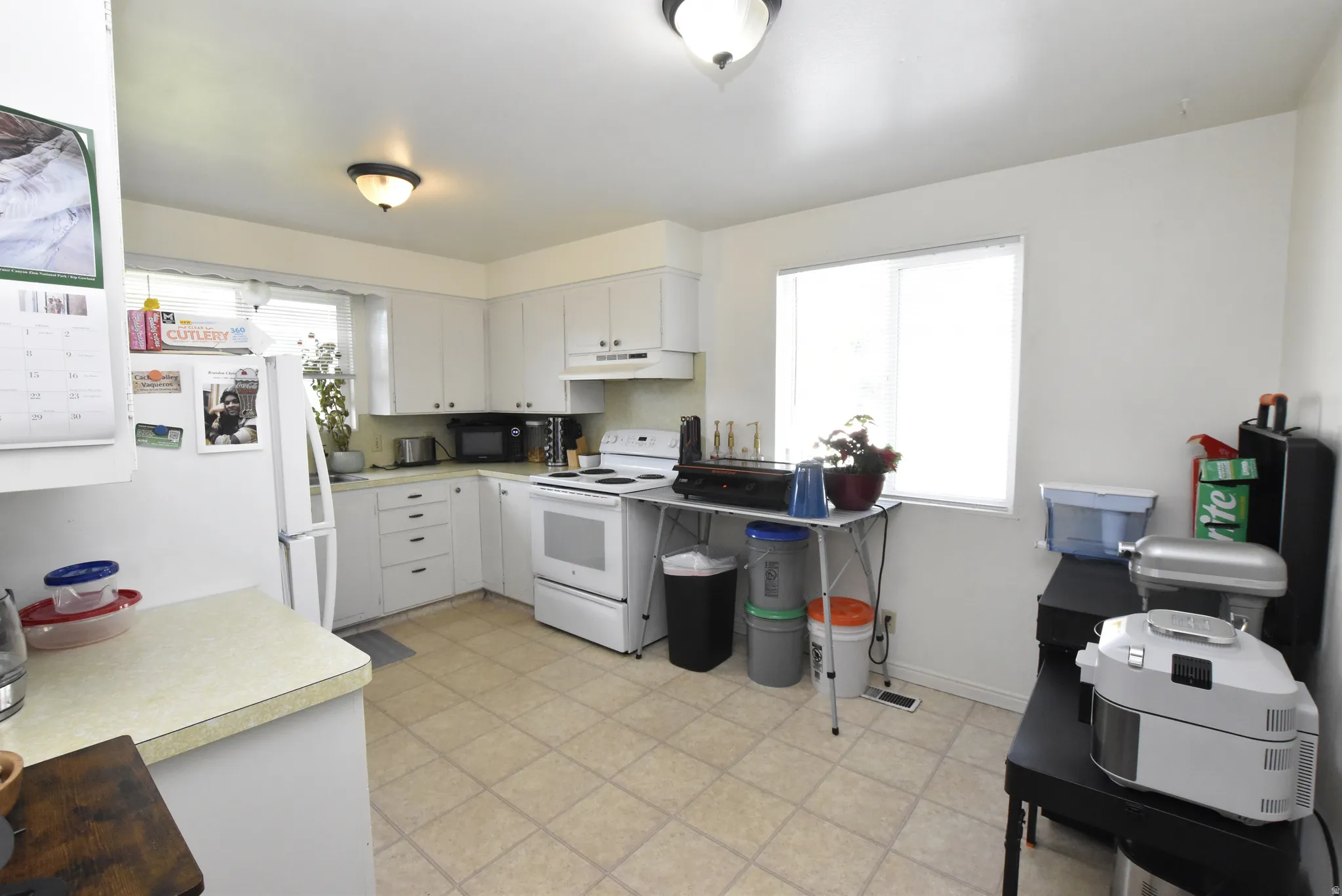 Well-lit kitchen featuring white cabinetry, a white electric range, and a white refrigerator