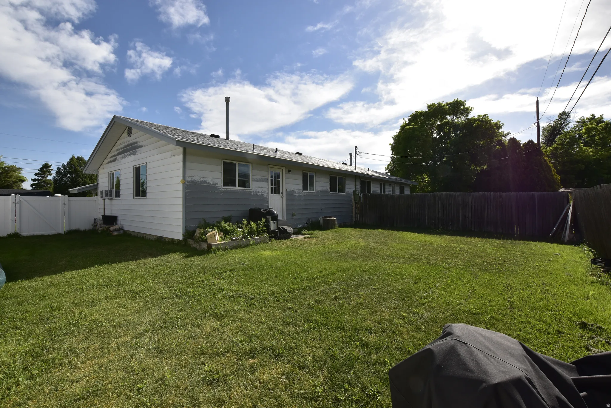 Expansive backyard featuring a manicured lawn, a full privacy fence, and a white vinyl fence section