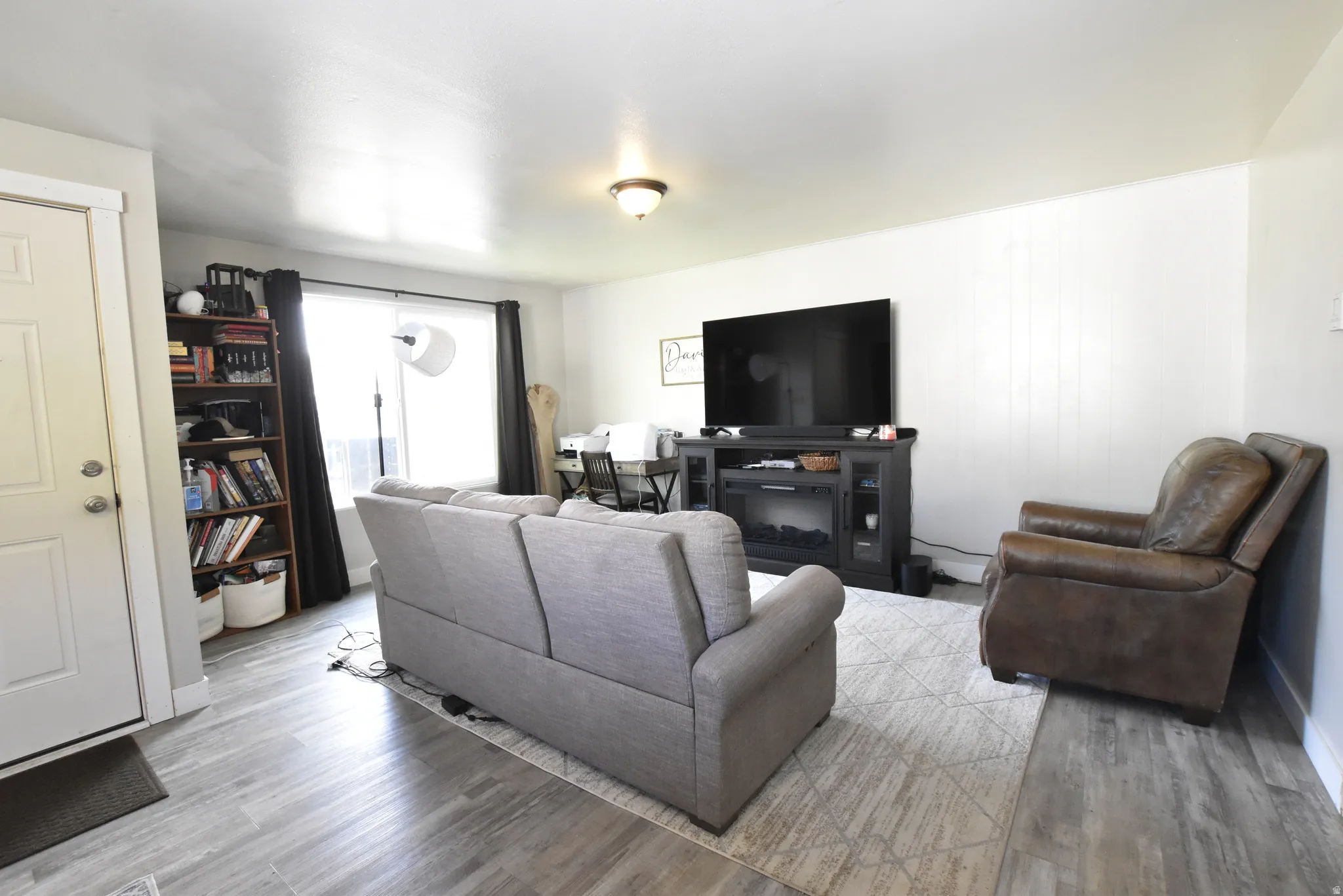Bright living area featuring wood-finish flooring, white walls, and a recessed window with dark curtains