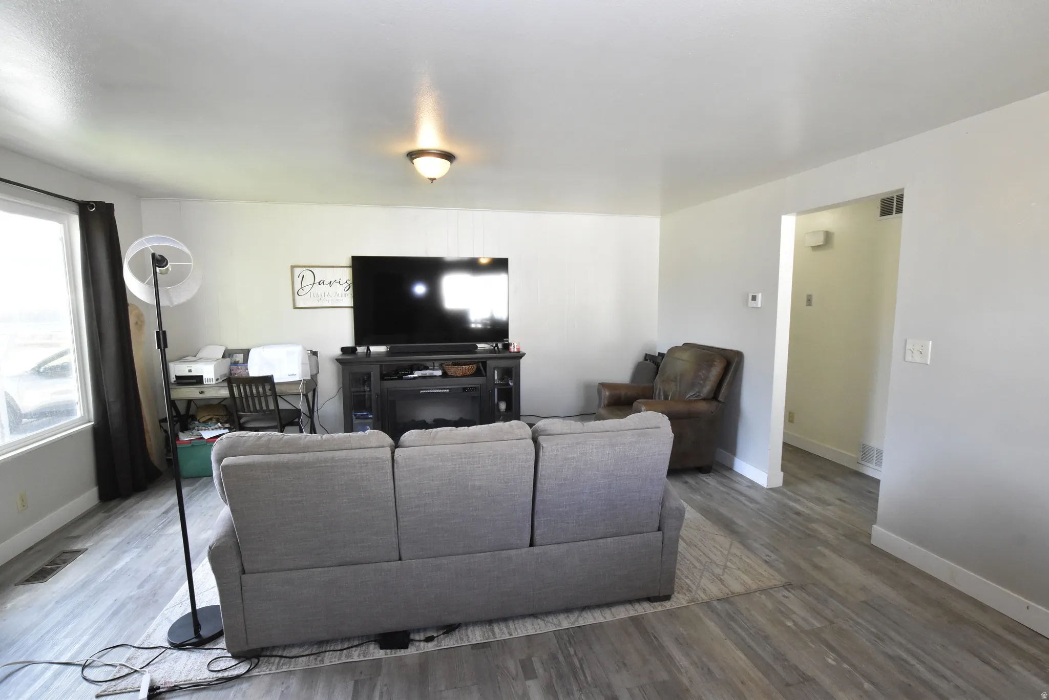 Spacious interior room featuring wood-finish flooring, light-toned walls, a large window, and an overhead light fixture