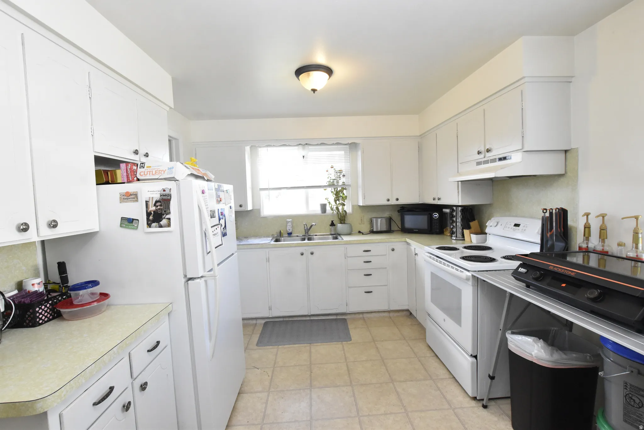 Kitchen featuring white cabinetry, light-toned countertops, a window over the sink, and tile flooring