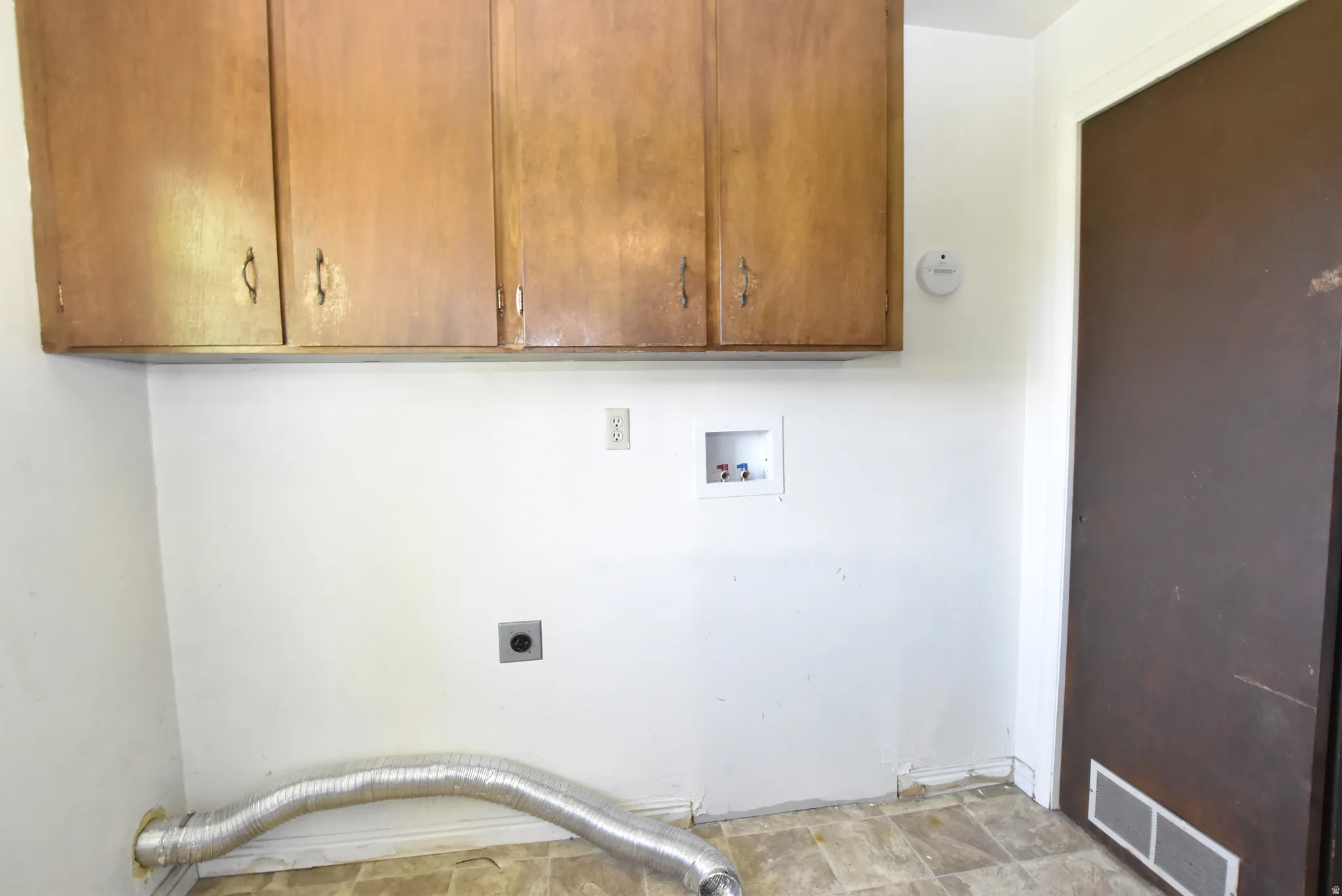 Utility space with wood-finish upper cabinetry, white walls, and vinyl flooring