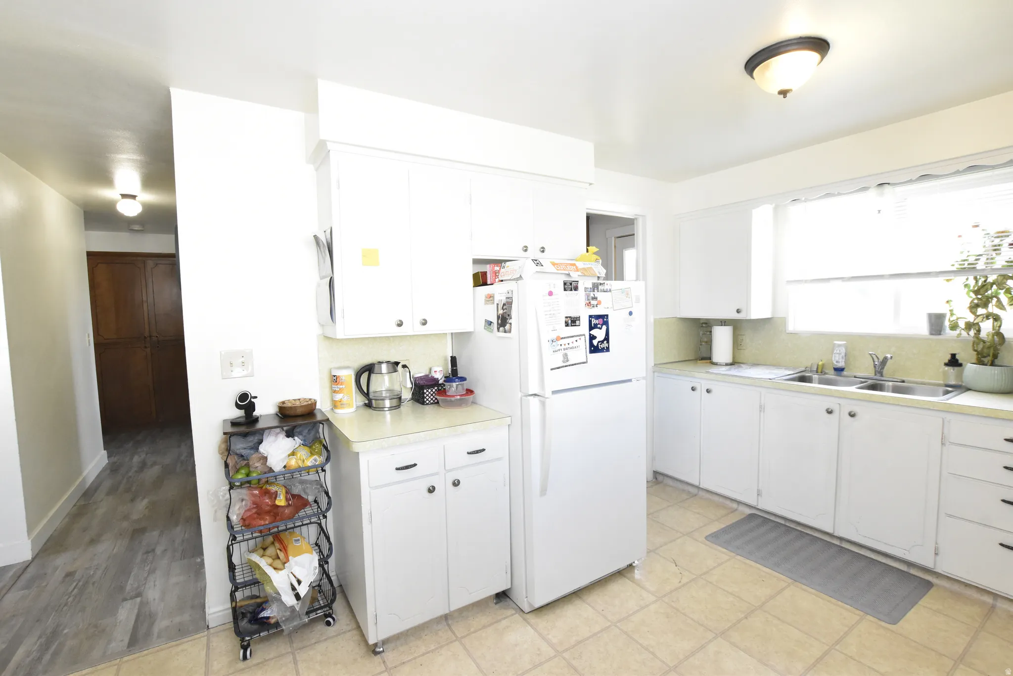 Kitchen featuring white cabinetry, a double basin stainless steel sink, a window over the sink, and tile flooring