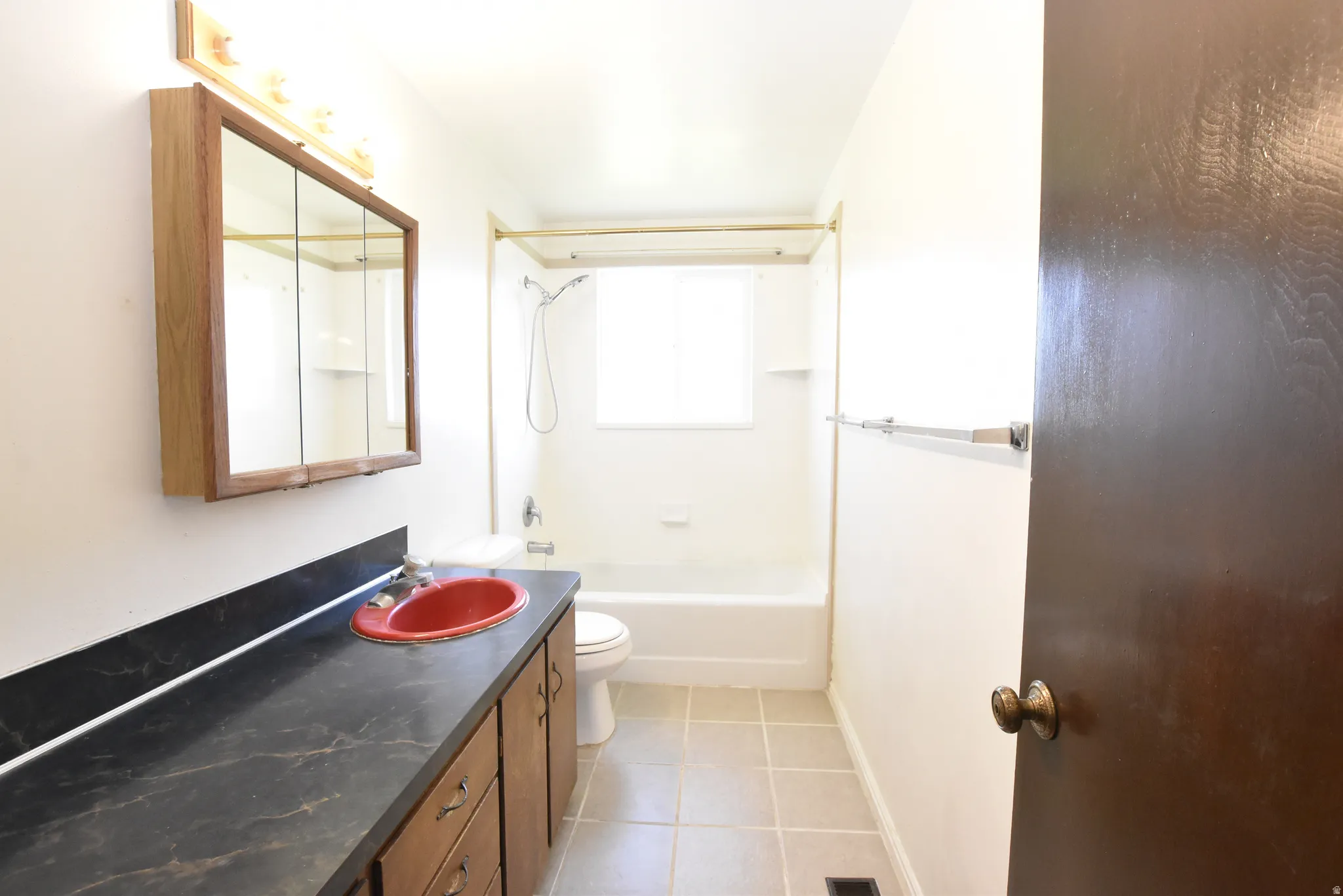 Bathroom featuring a lengthy vanity with a dark countertop and red basin sink