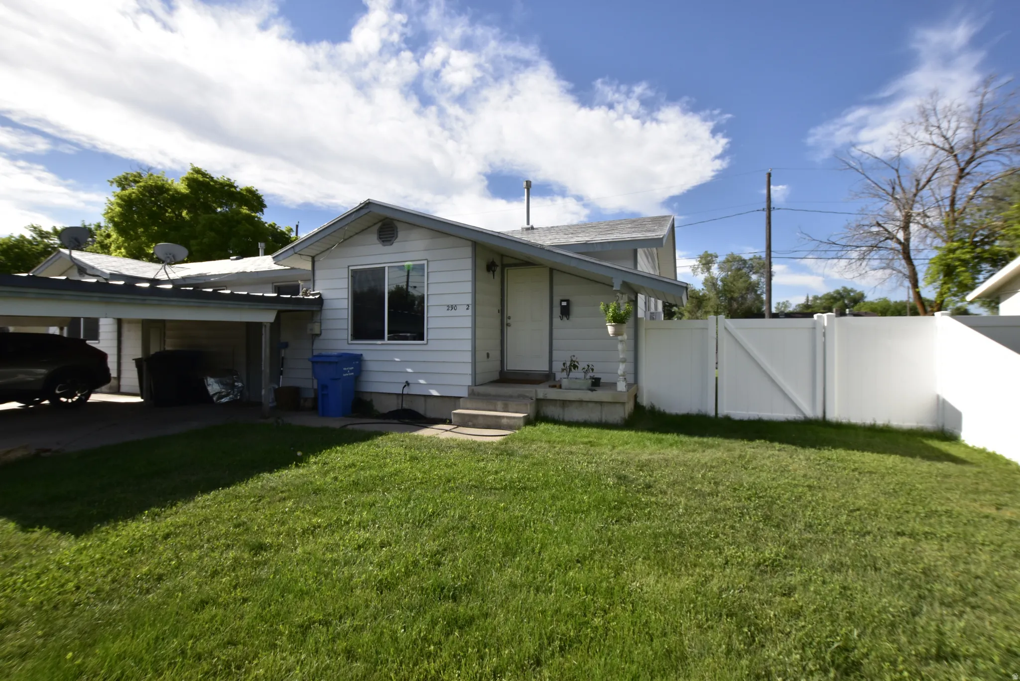 Single-story residence featuring white siding, a covered carport, and a white privacy fence