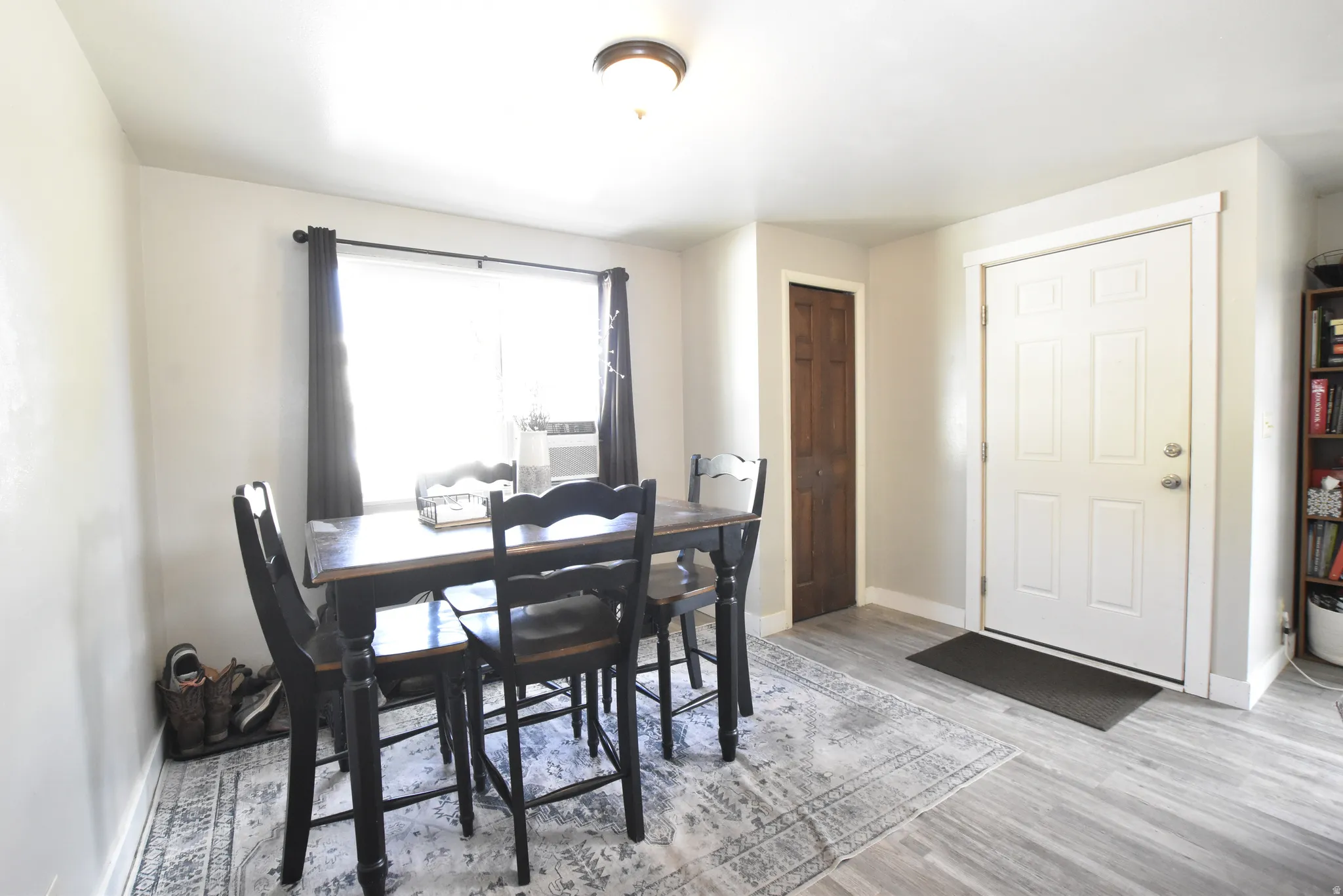 Dining area featuring a large window, light gray walls, wood-finish flooring, and a white paneled entry door