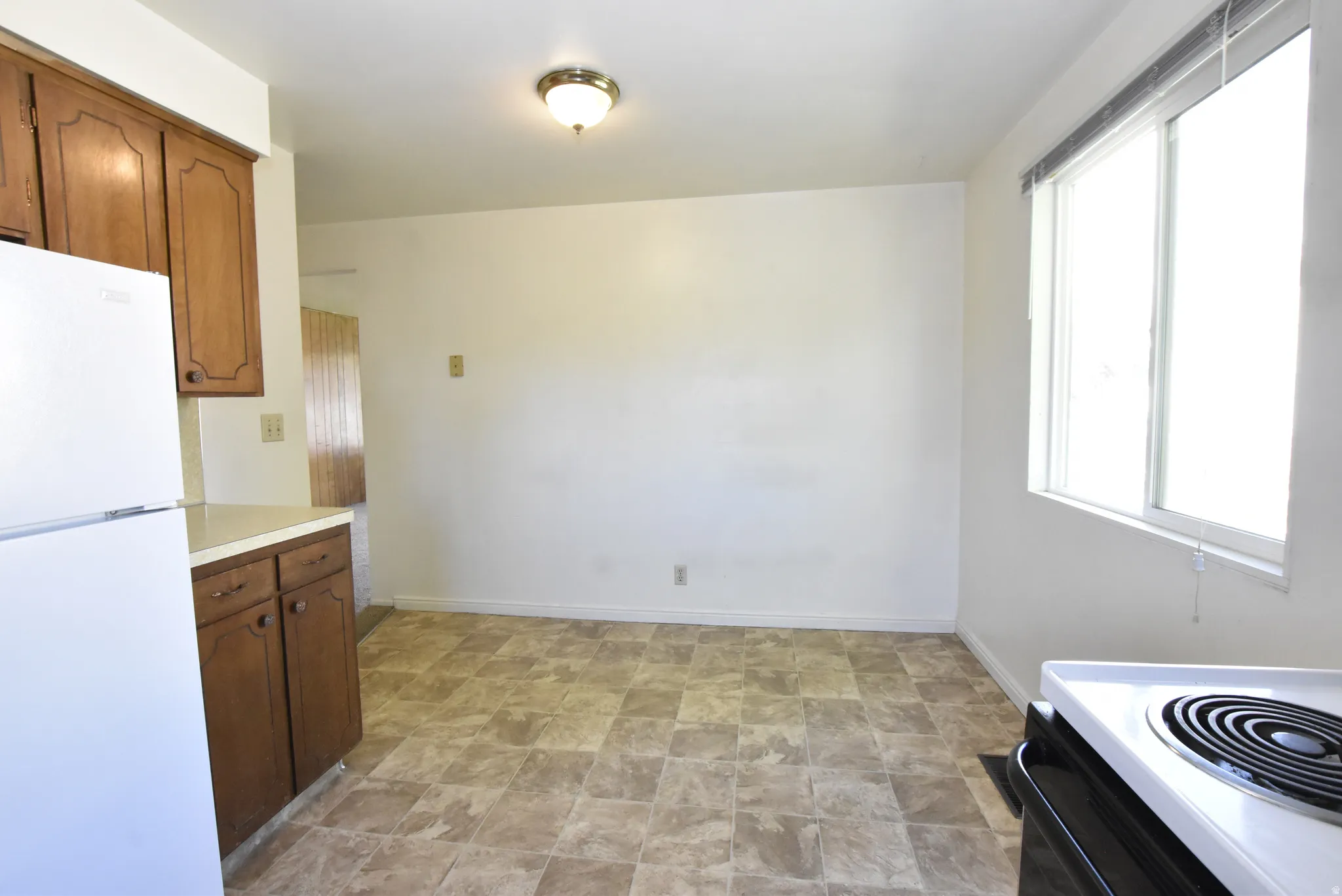 Kitchen space featuring a window, patterned floor tile, white walls, and a ceiling-mounted light fixture