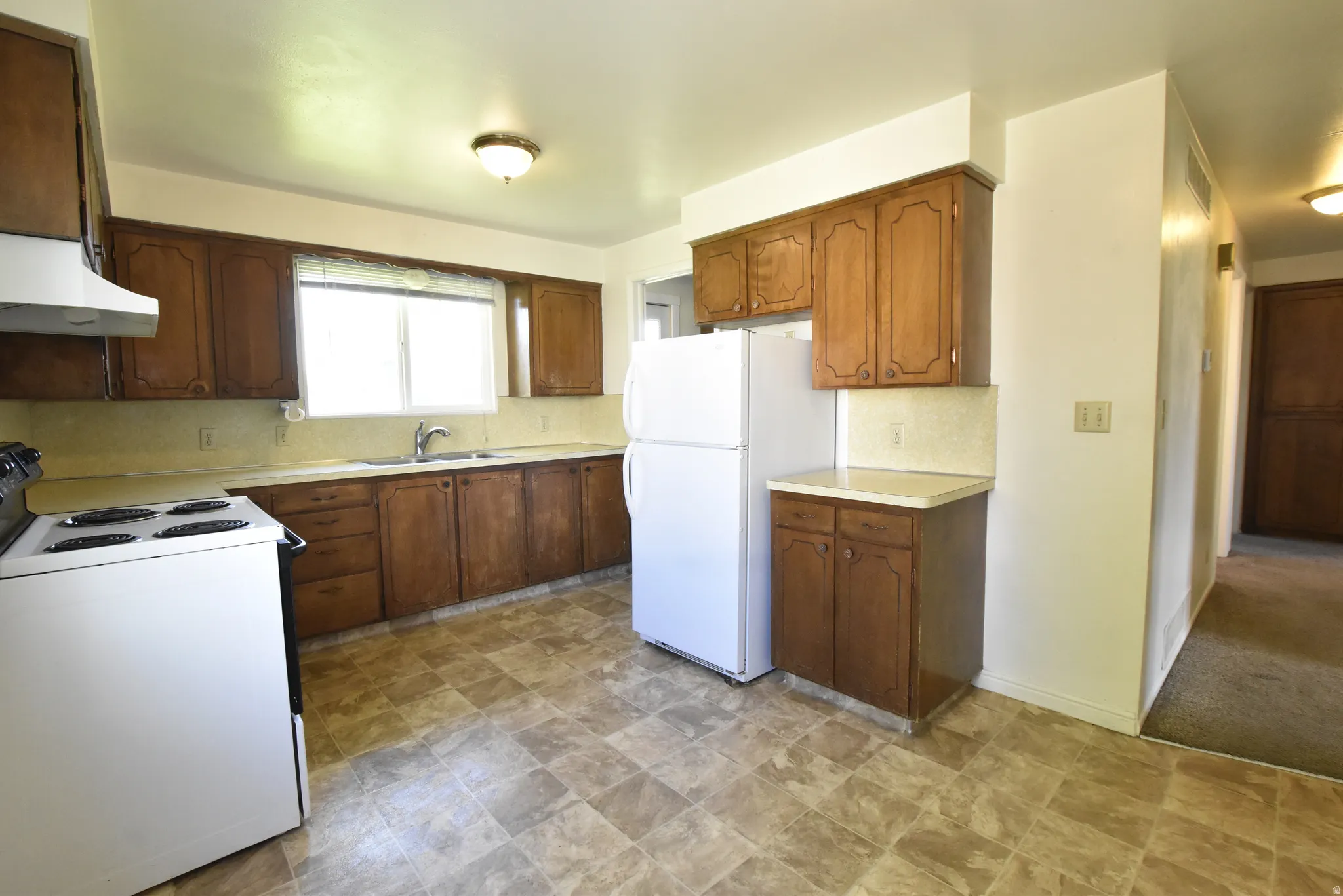 Kitchen featuring wood cabinetry, laminate countertops, a double basin sink, and tile-finish flooring