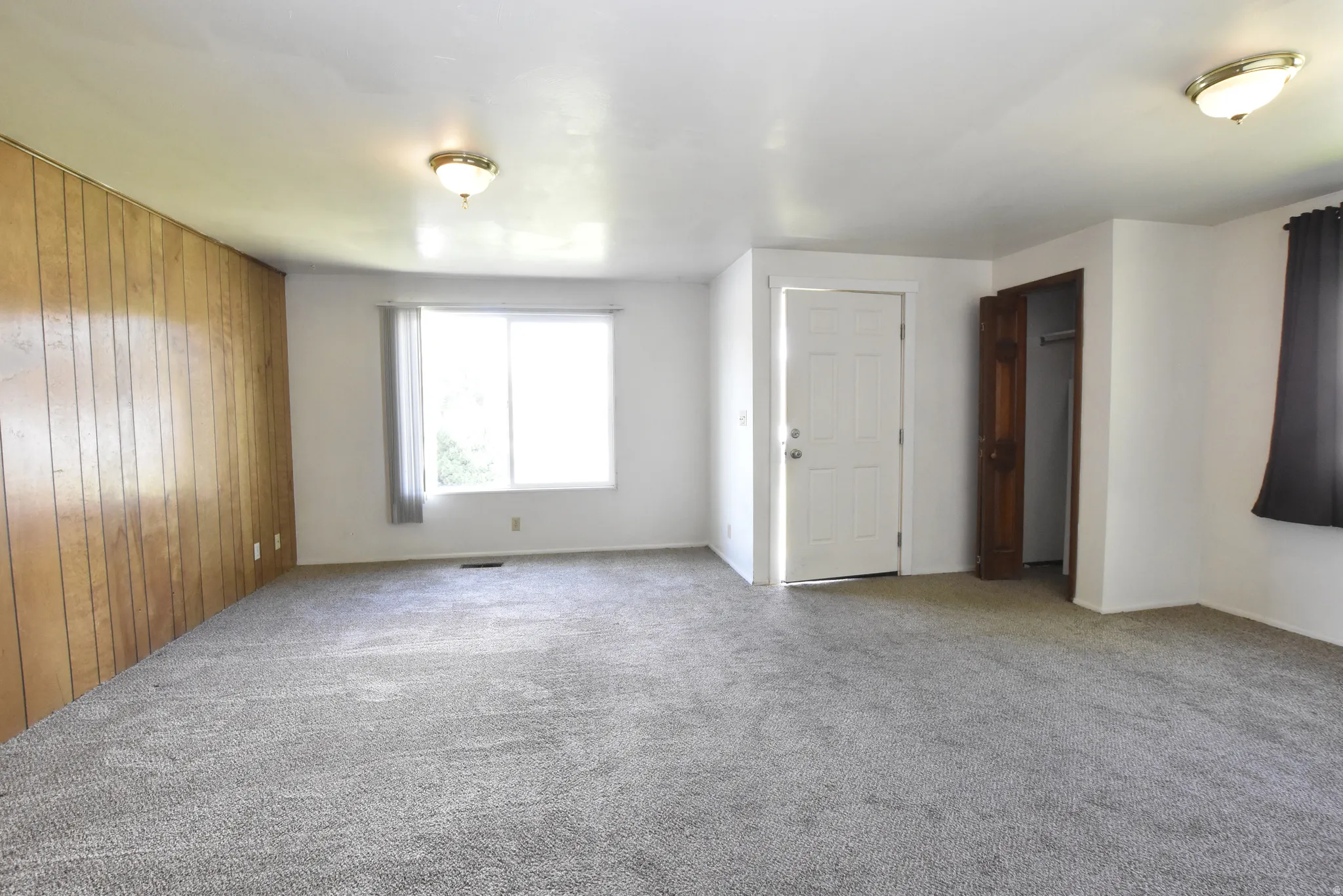 Spacious room featuring wood paneling, white painted walls, and gray carpet