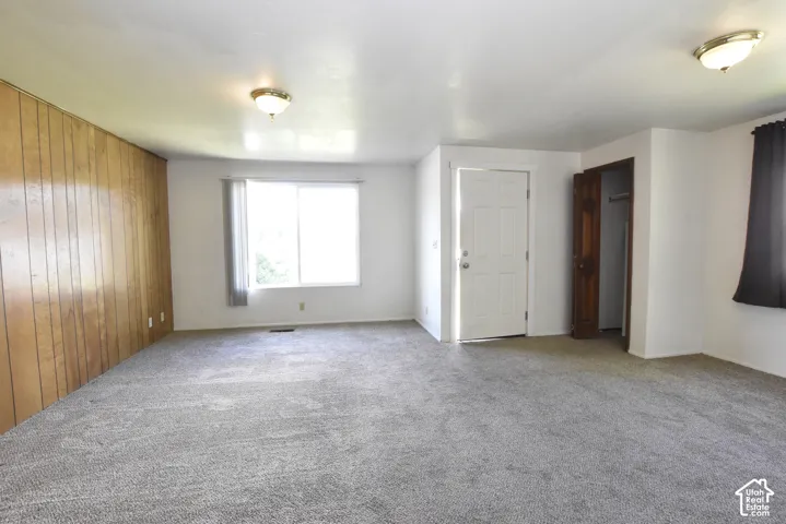Spacious room featuring wood paneling, white painted walls, and gray carpet