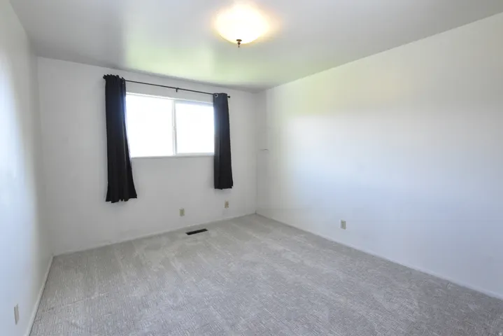 Bright interior space featuring a window with dark drapes, light-colored carpeting, white wall finishes, and a flush-mount ceiling light fixture