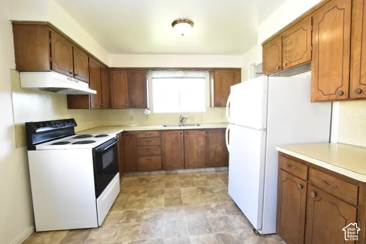 Kitchen featuring wood-finish cabinetry, white appliances, and a window above the sink