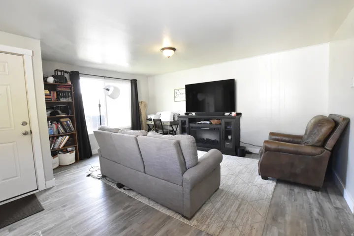 Bright living area featuring wood-finish flooring, white walls, and a recessed window with dark curtains
