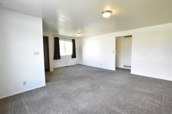 Spacious room featuring gray carpet, white walls, and a large window with black window treatments