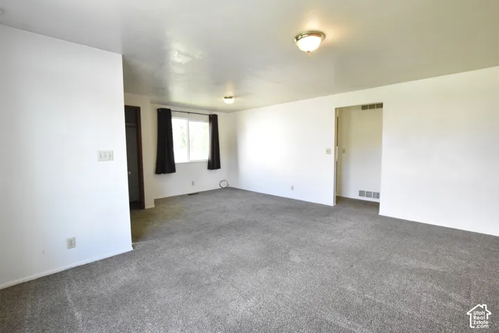 Spacious room featuring gray carpet, white walls, and a large window with black window treatments