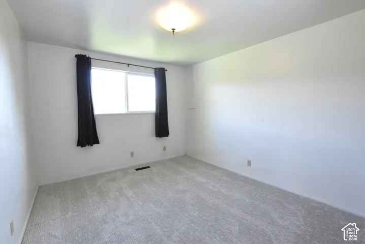 Bright interior space featuring a window with dark drapes, light-colored carpeting, white wall finishes, and a flush-mount ceiling light fixture